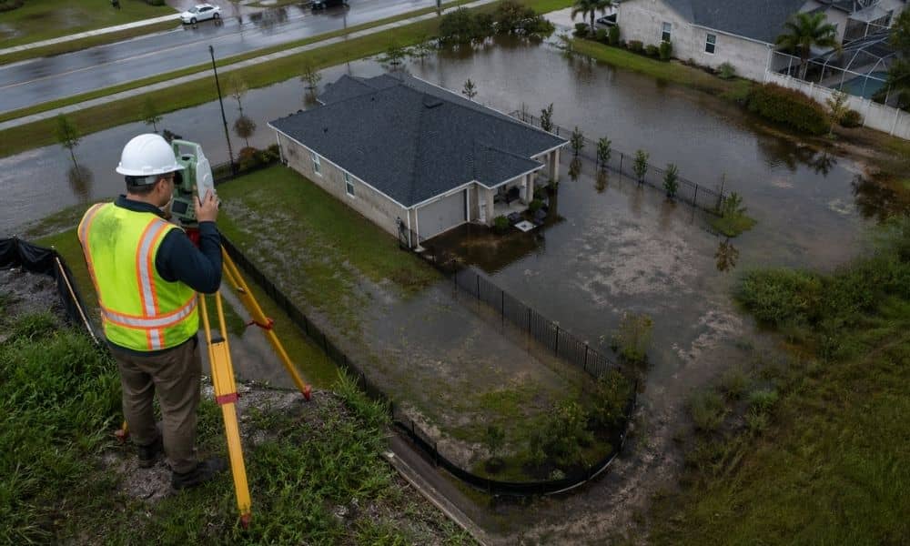 Aerial view of a flooded residential area with a surveyor using equipment on uneven ground, showing how land surveys help reveal elevation changes and flood risk in neighborhoods