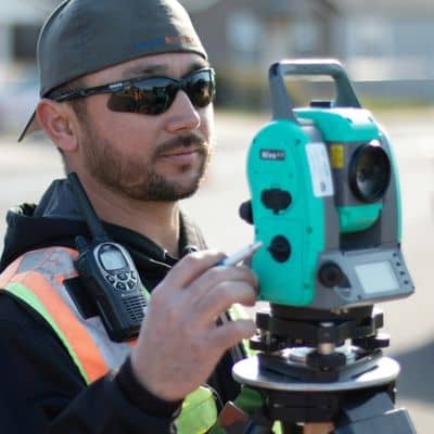 Close-up of a land surveyor using a total station on a residential site to measure elevation and ground levels for accurate land surveys and flood risk assessment.