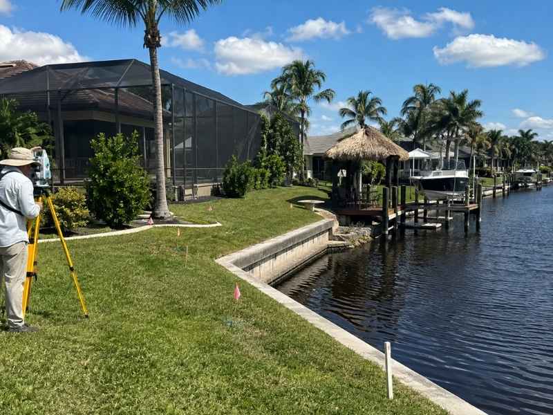 Boundary survey cost for an irregular canal-side lot in Fort Myers Florida, showing a surveyor measuring a waterfront property with a seawall and dock.