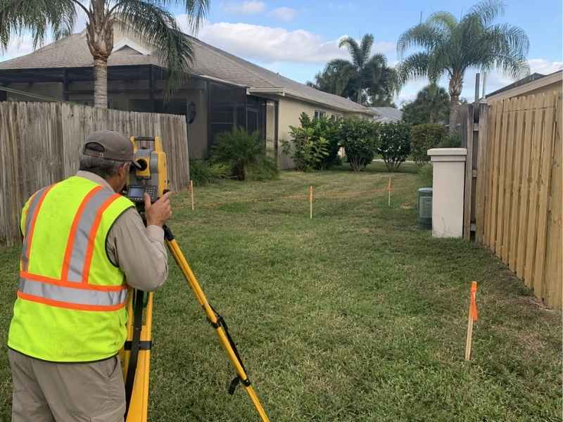 Property survey for fence work in Fort Myers Florida showing a surveyor measuring connection points between existing side fences.