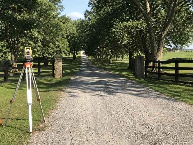 Land surveying equipment beside a long private gravel access road on a wooded property in Fort Myers, Florida.